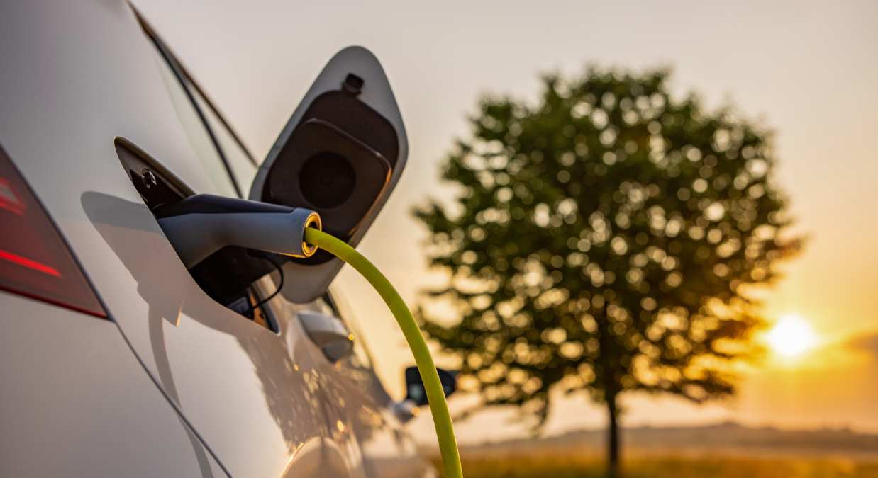 Electric car charging with tree and sunset in background