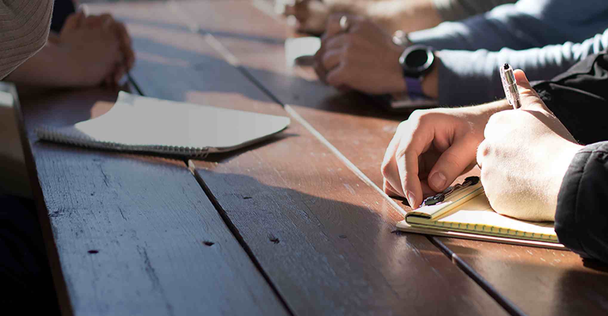 Close up of a desk with four people writing on notepads