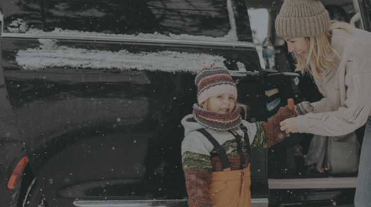 Mother and child next to a black car in snowy weather